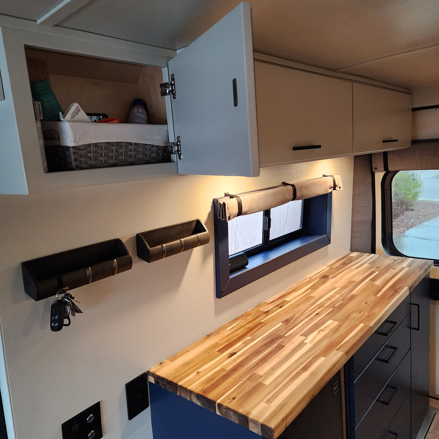 This RV rental features a modern interior with light cabinets, open storage, a window with shade, and a butcher block counter.