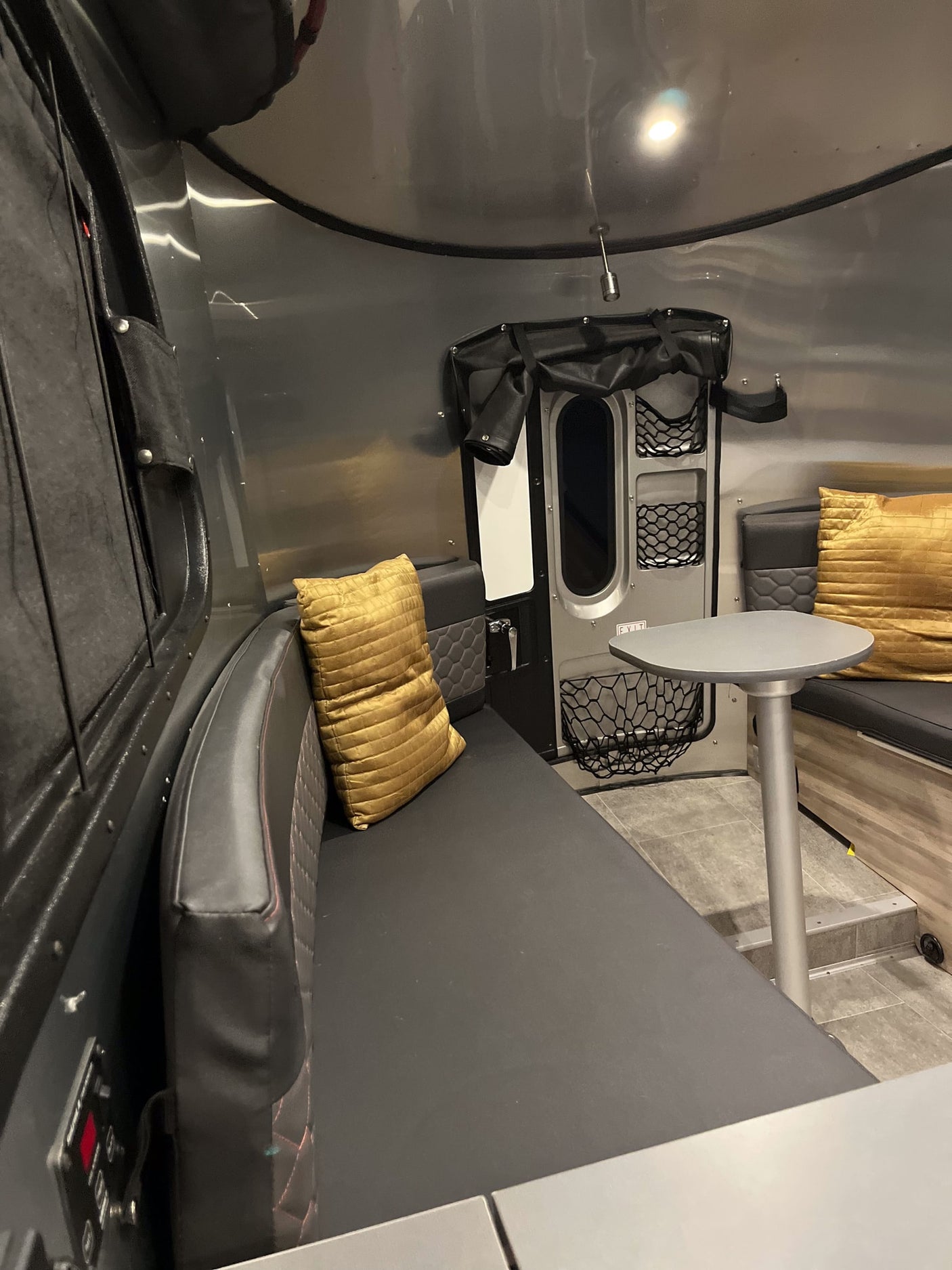 Modern RV rental interior with sleek black seating, gold pillows, and a dining table, showcasing compact living space.