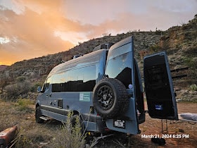 is parked with interior lights on at an evening forest campsite.|Stargazing from an RV rental: a silver van under the stunning Milky Way galaxy at night. Perfect for adventure.|Gray RV rental camper van at sunset — photo 6