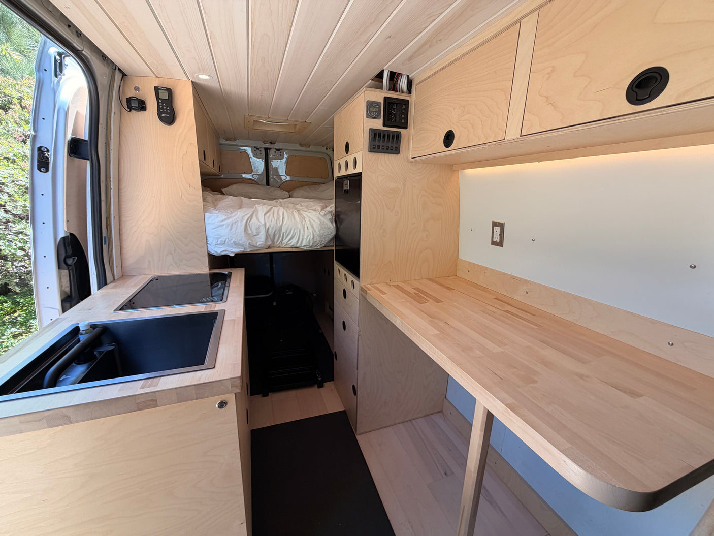 Spacious rv rental interior featuring a wood-paneled van conversion with a kitchenette, bed, and work counter for comfortable travel.