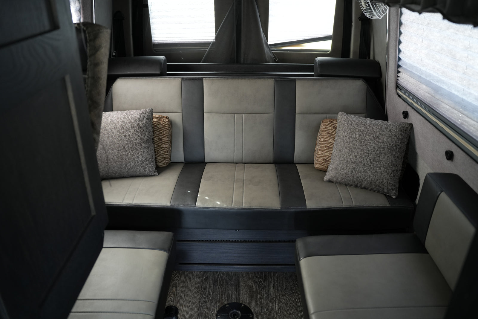 Comfortable gray and black seating in an RV rental, with patterned pillows, window blinds, and dark wood-look flooring.