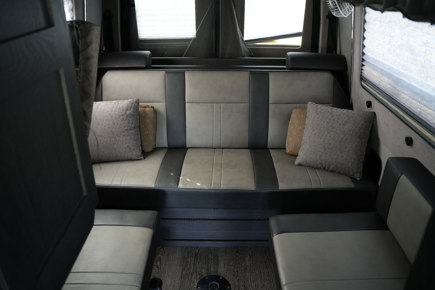 Comfortable gray and black seating in an RV rental, with patterned pillows, window blinds, and dark wood-look flooring.
