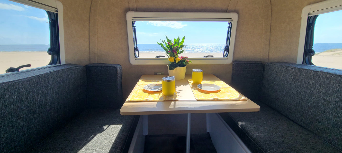 Enjoy beach views from your RV rental: a cozy dining area with two place settings, a flower vase, and ocean scenery.