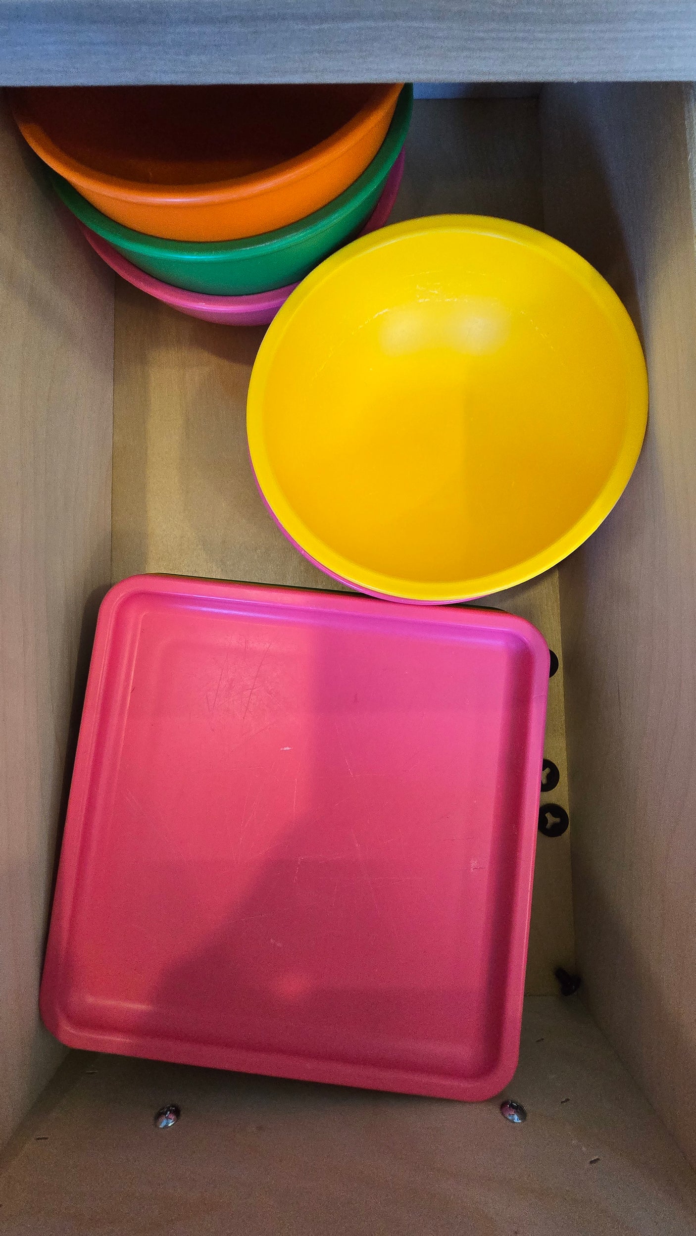 Bright plastic bowls & a pink tray in an RV rental drawer, perfect for compact kitchen storage.