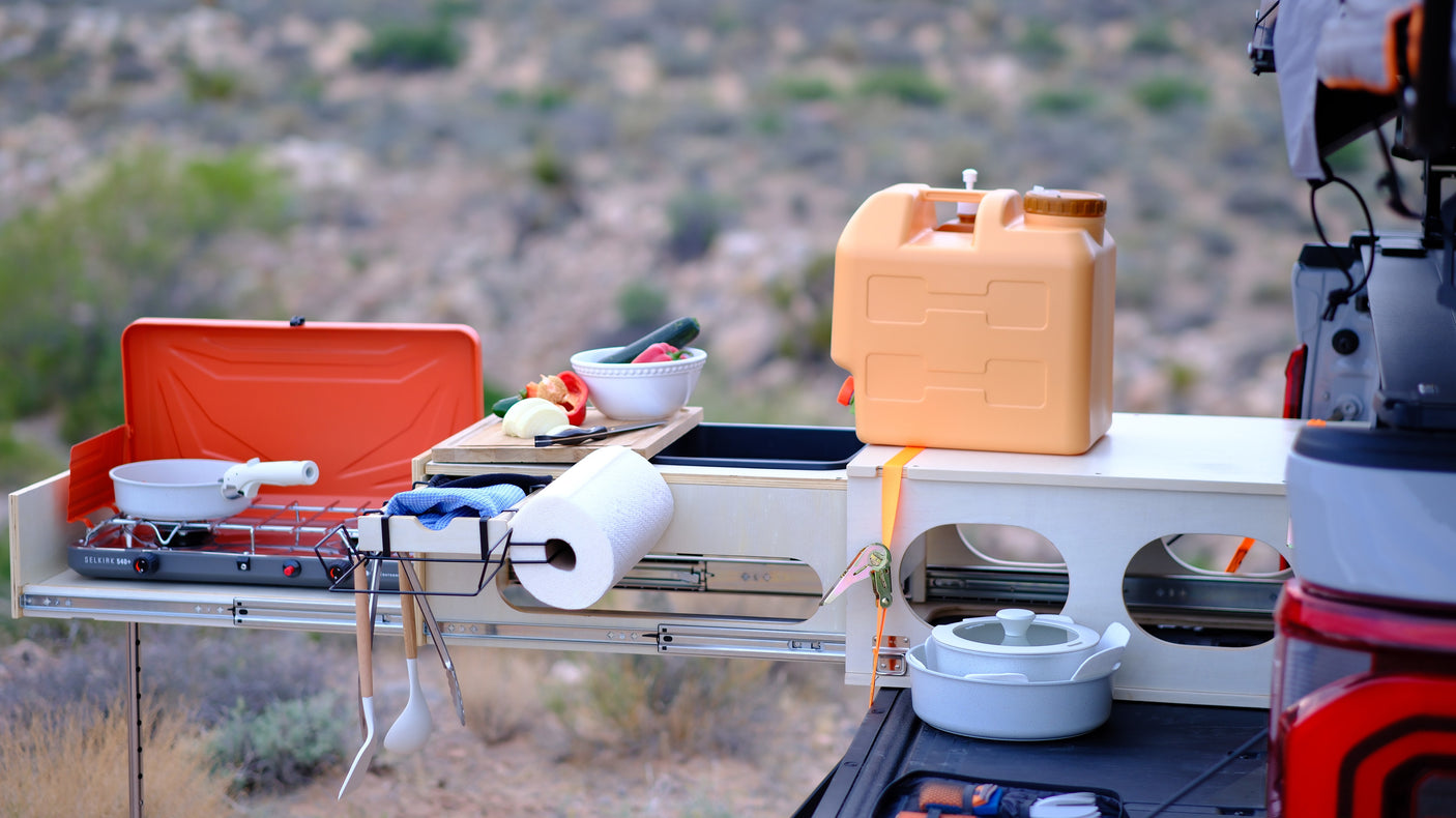 This RV rental features a convenient slide-out camping kitchen with a stove, water jug, veggies, and cooking gear for outdoor meals.
