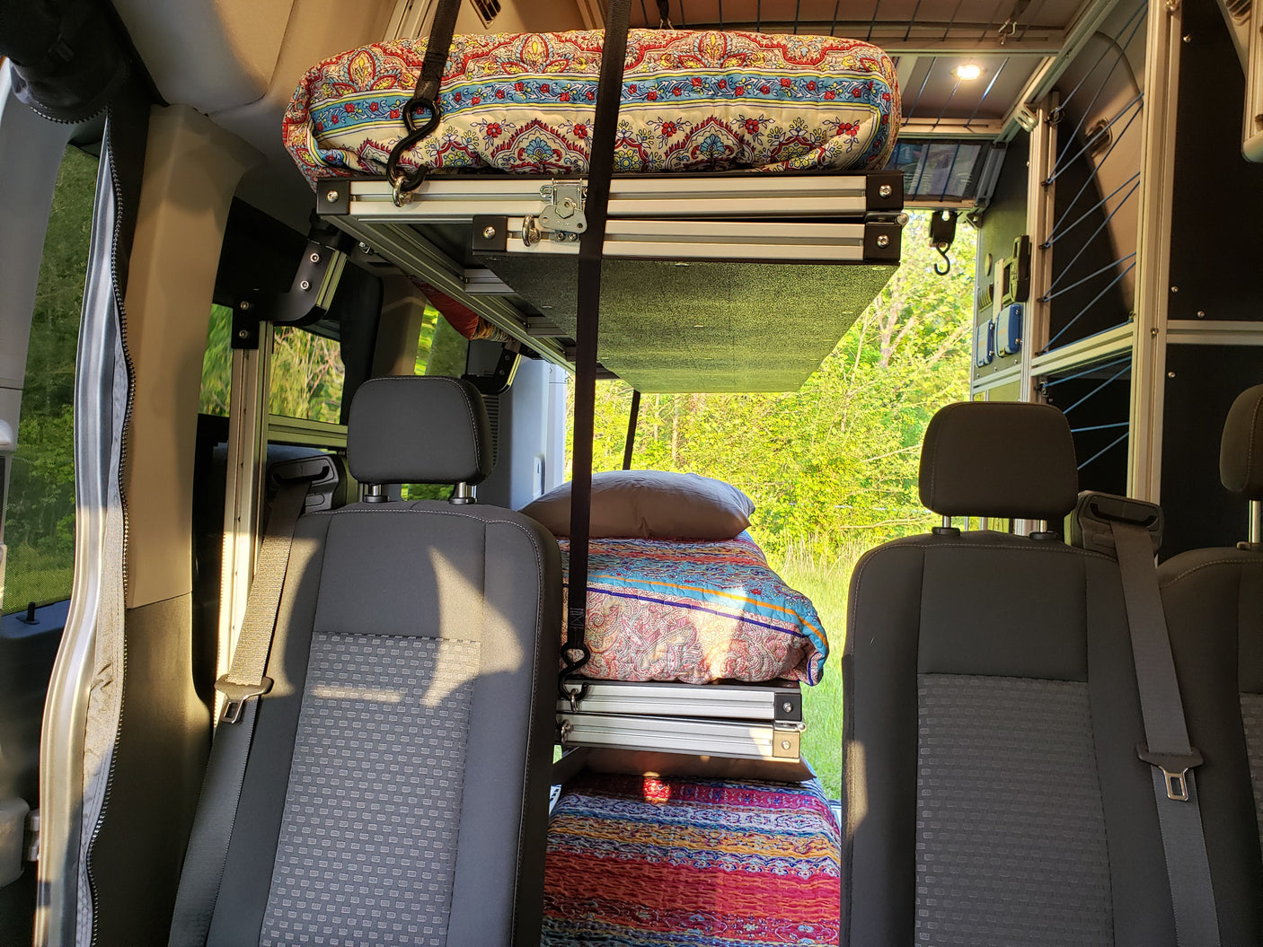 Inside an RV rental: a unique adjustable bed system with two cozy sleeping levels, colorful bedding, and front vehicle seats.