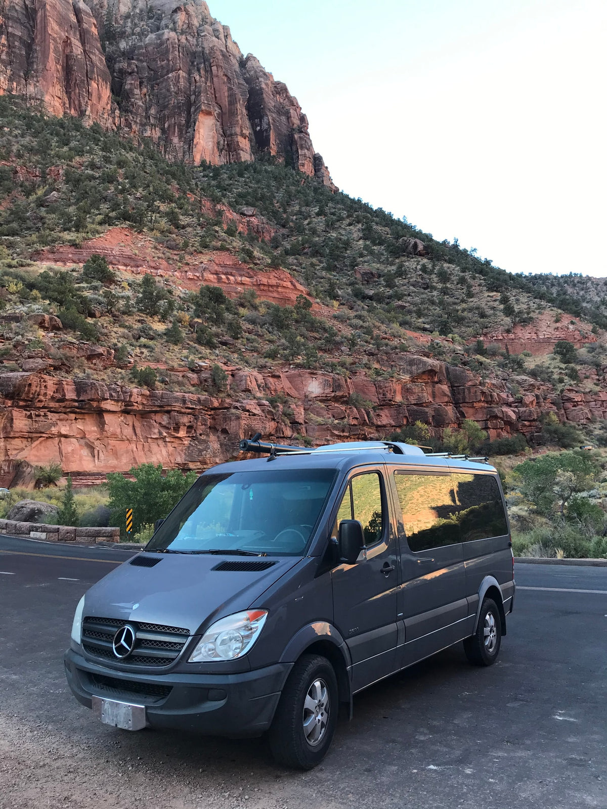 Exploring scenic landscapes with an rv rental: a gray Mercedes Sprinter camper van parked by massive red cliffs.|Dark grey RV rental (Mercedes Sprinter) parked with stunning red rock mountains & clear blue sky background.|Gray Mercedes Sprinter van