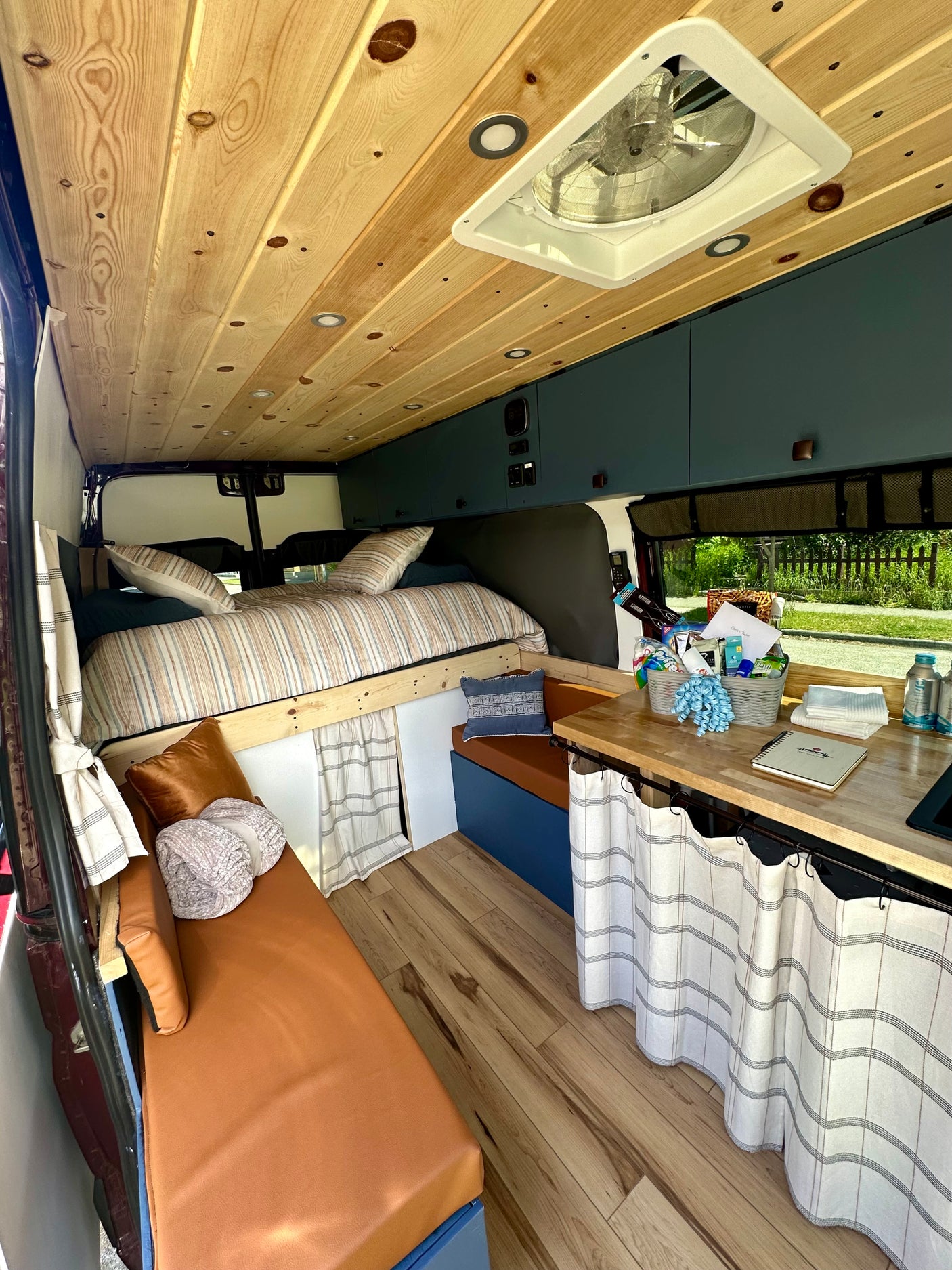Spacious RV rental interior featuring a wooden ceiling, elevated bed, and counter area. A cozy, functional camper van setup.