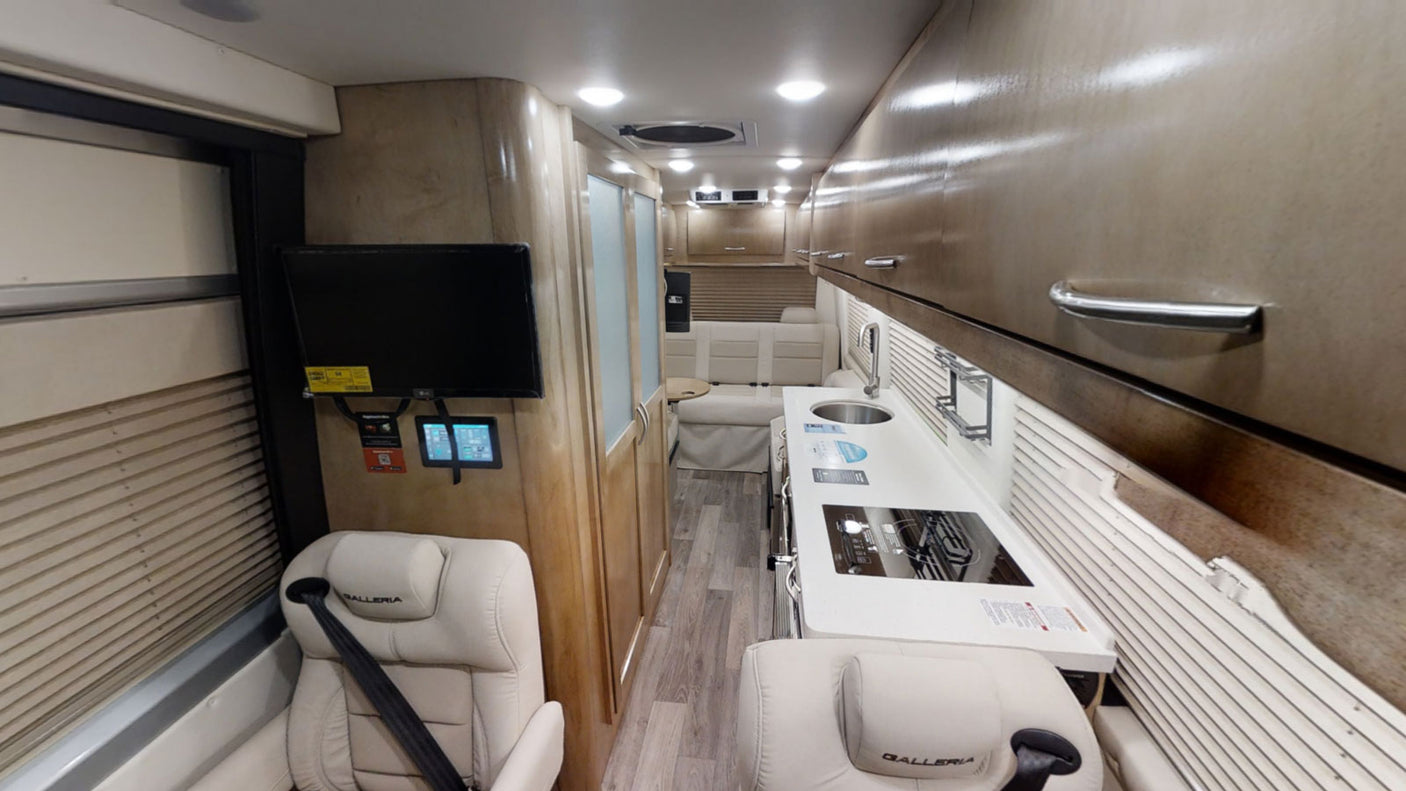 Step inside this comfortable RV rental. Features include a compact kitchen with sink/stove, cream seating, and a mounted TV.