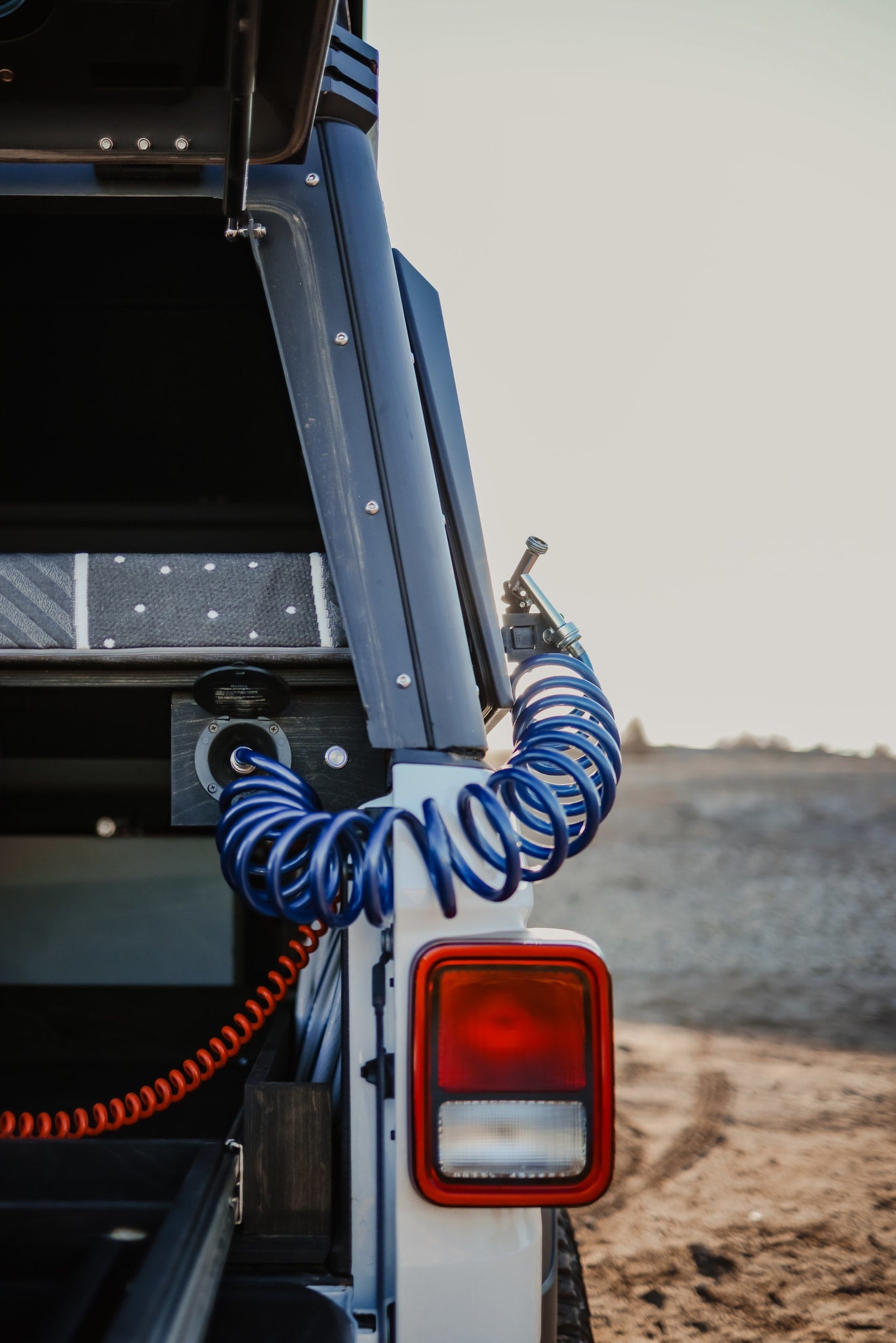 Close-up of an RV rental's rear utility area: blue coiled air/water hose, port, orange wire, and red taillight. Ideal for adventure. — photo 18