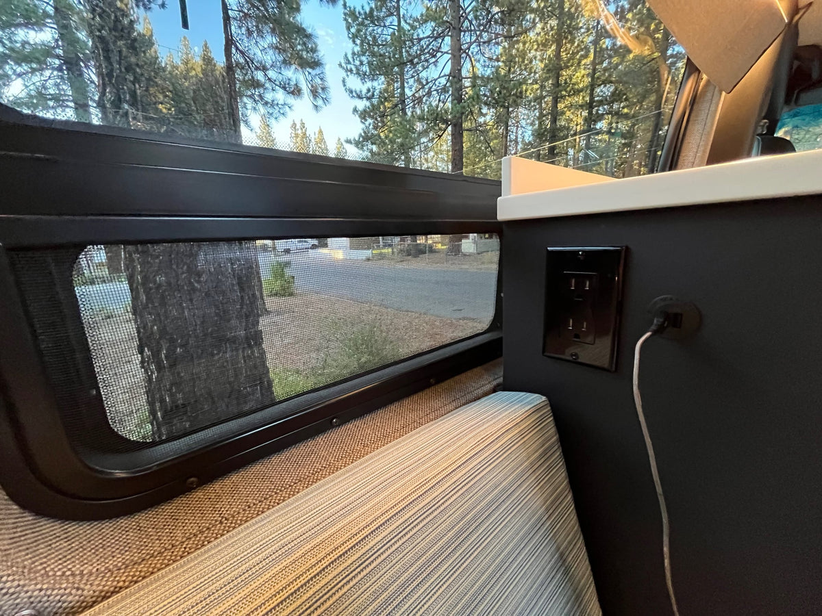 parked among trees.|Cozy camper van interior for your next RV rental adventure. Features a comfortable bed — photo 9