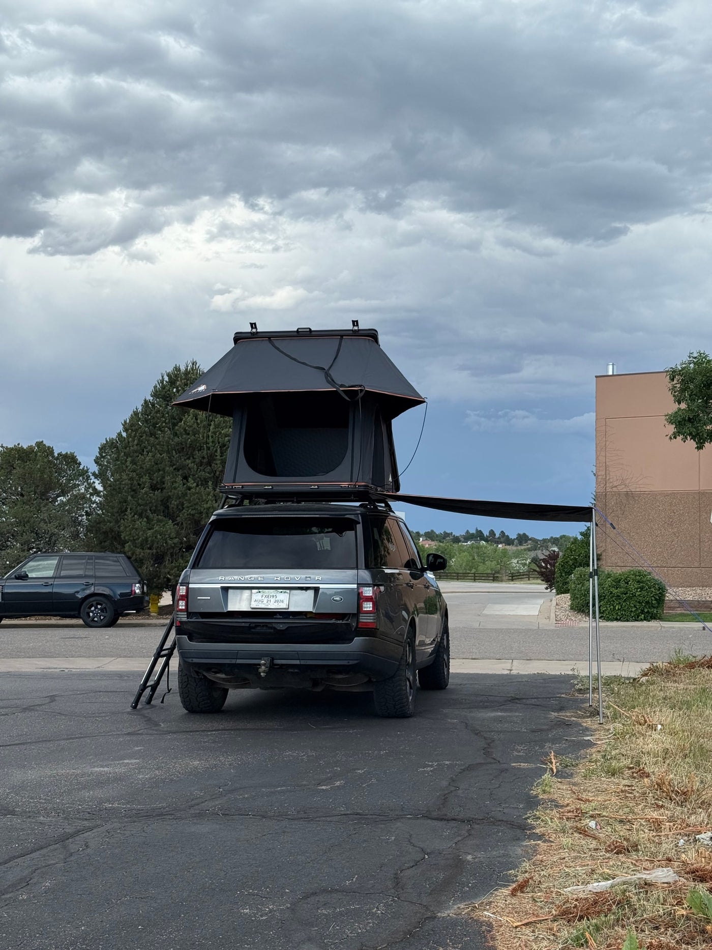 A grey Range Rover SUV with a rooftop tent, ladder, and side awning, ready for your next RV rental overland adventure. — photo 4