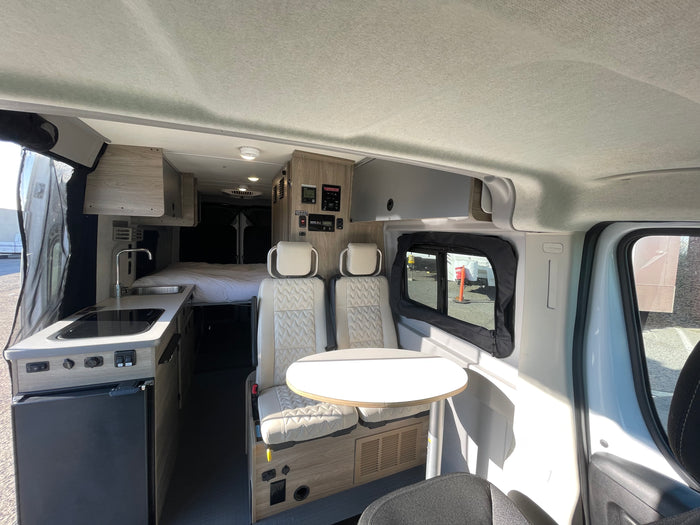 Modern rv rental interior featuring a compact kitchen, comfortable bed, and versatile seating with a table.