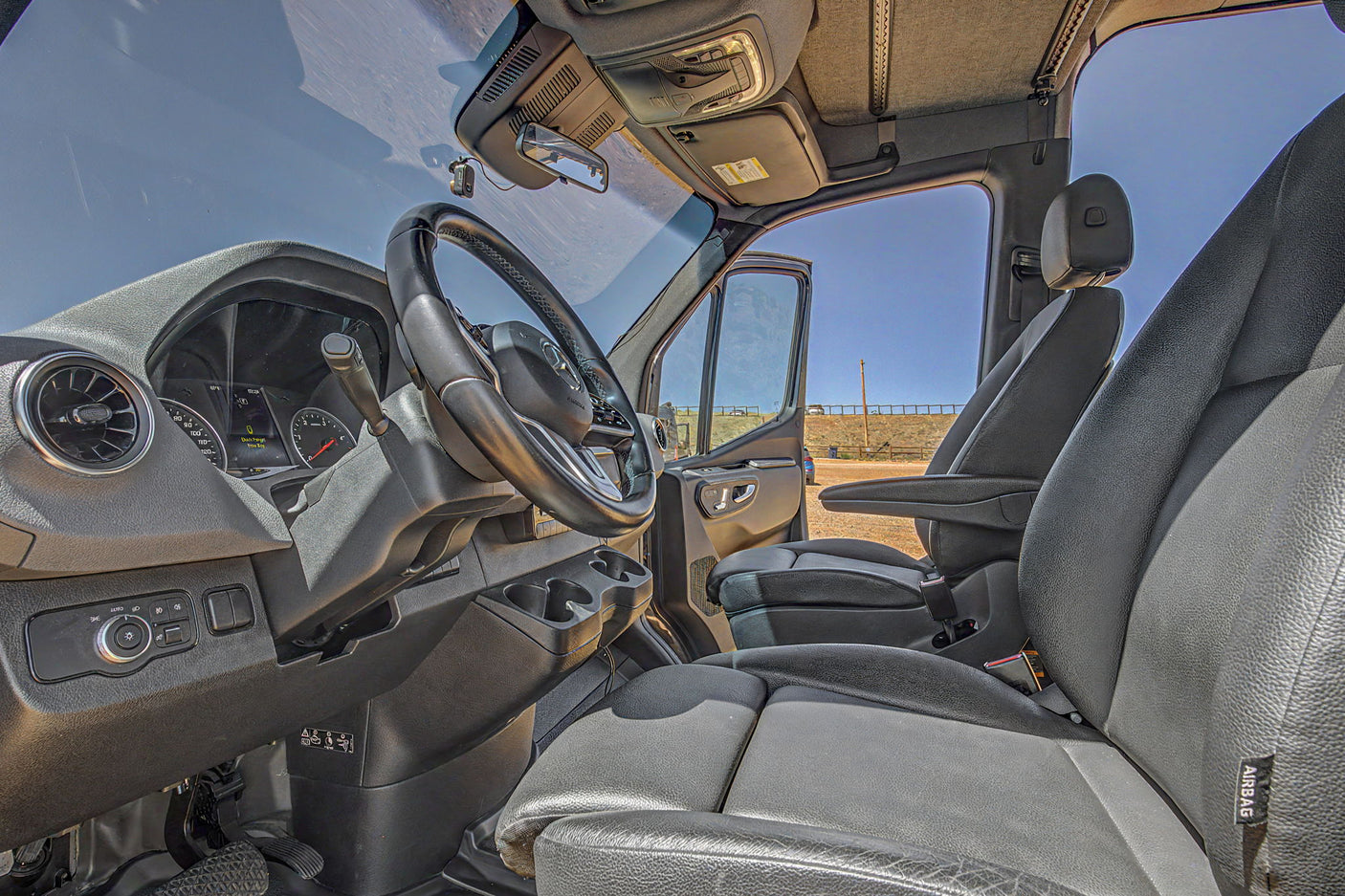 Driver's perspective inside an RV rental van, highlighting the steering wheel, dashboard, and black leather seats.
