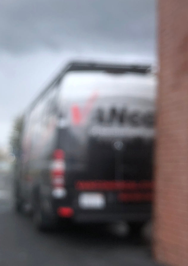 Extremely blurry black van, potentially an RV rental, parked by a brick wall. Red taillights are visible on the vehicle.