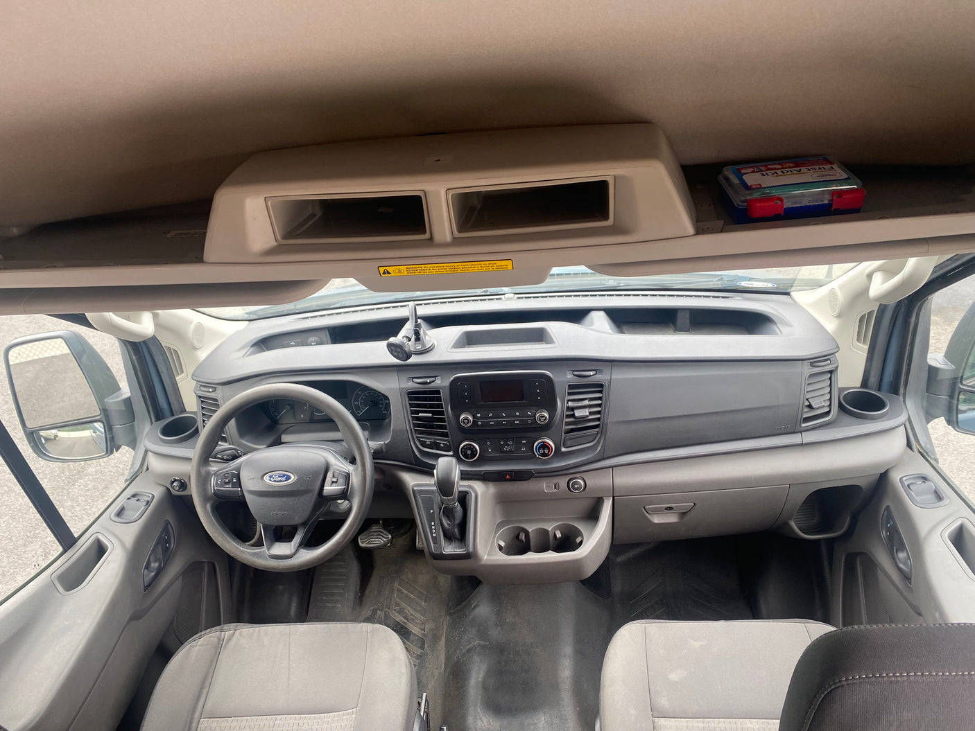 Inside an RV rental van: Ford dashboard, steering wheel, gear shift, and overhead storage with a visible first aid kit.