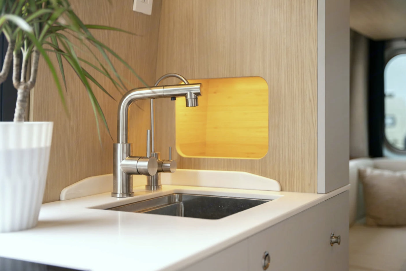 RV rental: A bright, compact kitchen area with a sleek brushed silver faucet, integrated sink, and light wood paneling.