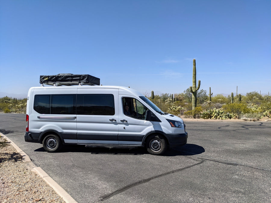 under a serene sunset.|White camper van RV rental parked on a desert road with saguaro cacti under a clear blue sky