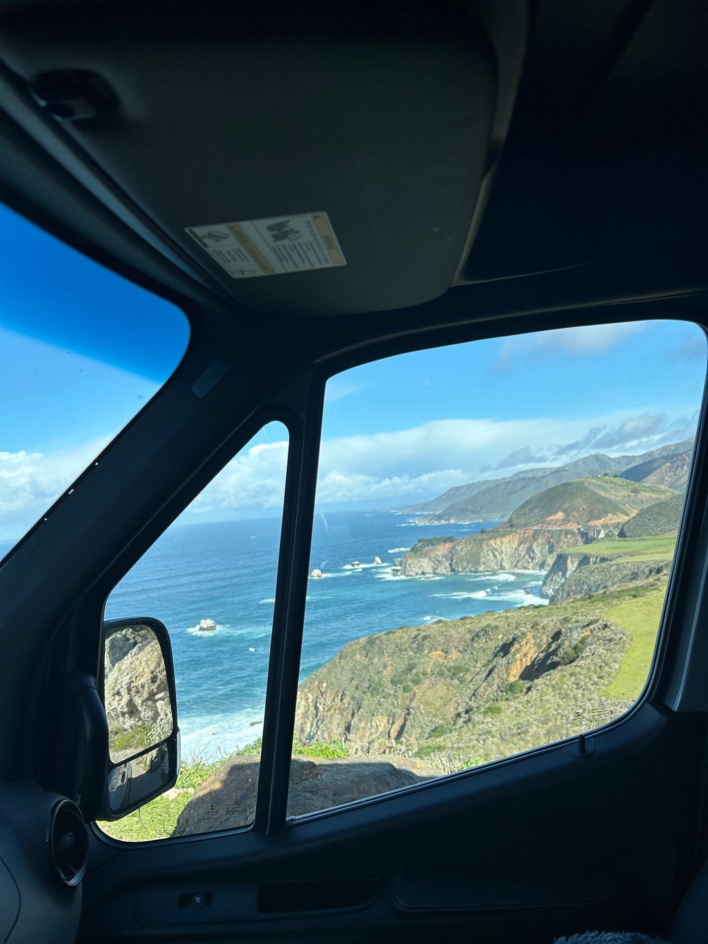 View from an RV rental of a stunning coastal landscape with ocean, cliffs, & green hills.