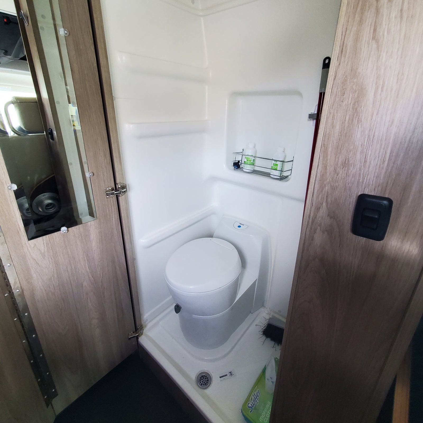 Inside an RV rental: a compact bathroom with a white toilet, integrated shower stall, wood-look doors, and a shower caddy.