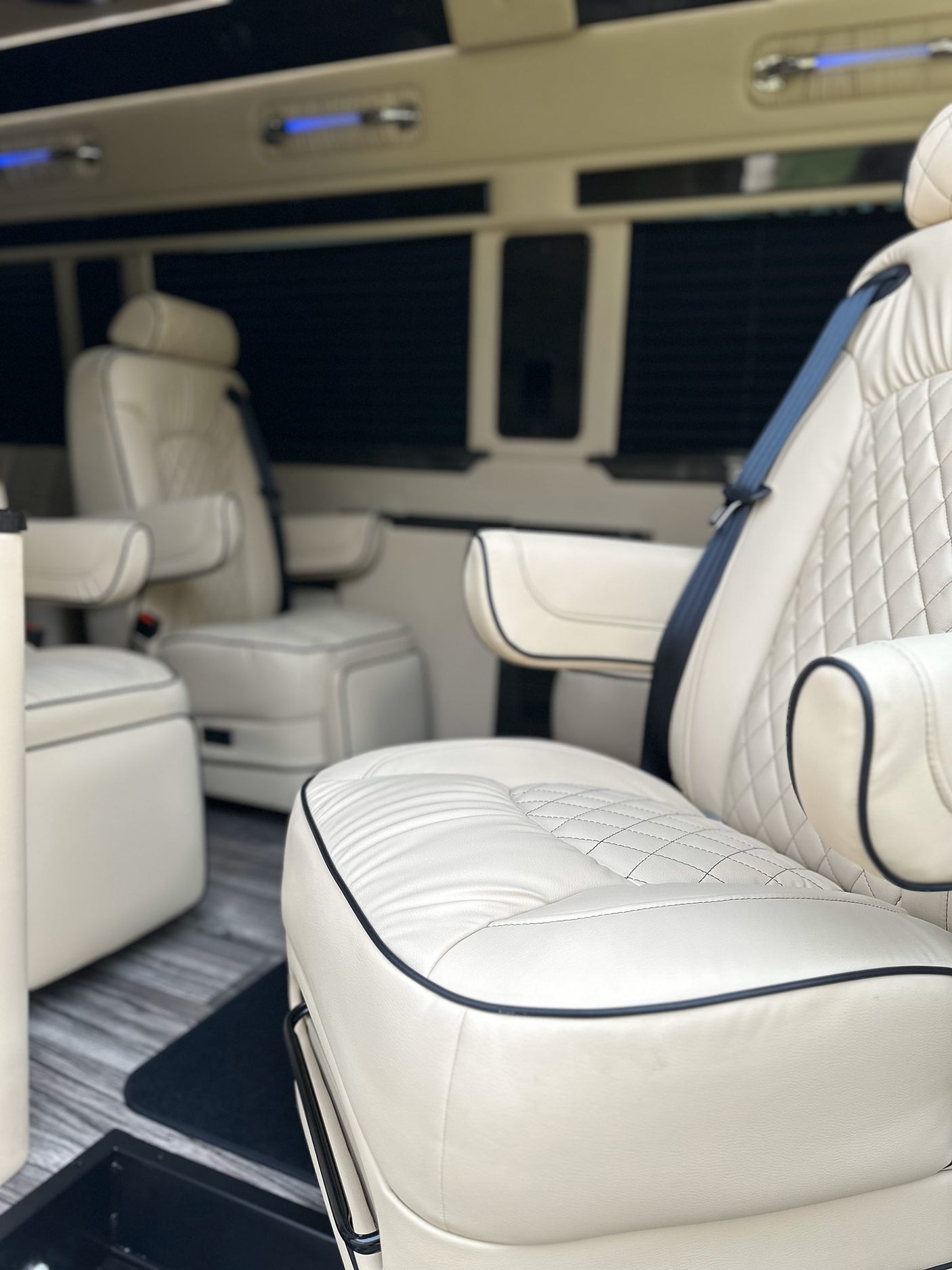 Luxury RV rental interior: cream quilted leather seats with armrests and blue overhead lighting for premium travel.