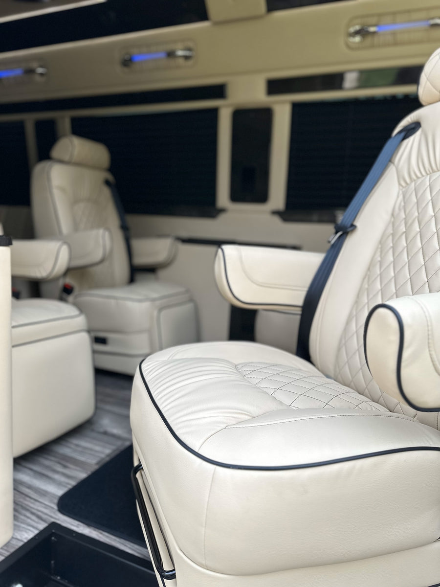 Luxury RV rental interior: cream quilted leather seats with armrests and blue overhead lighting for premium travel.