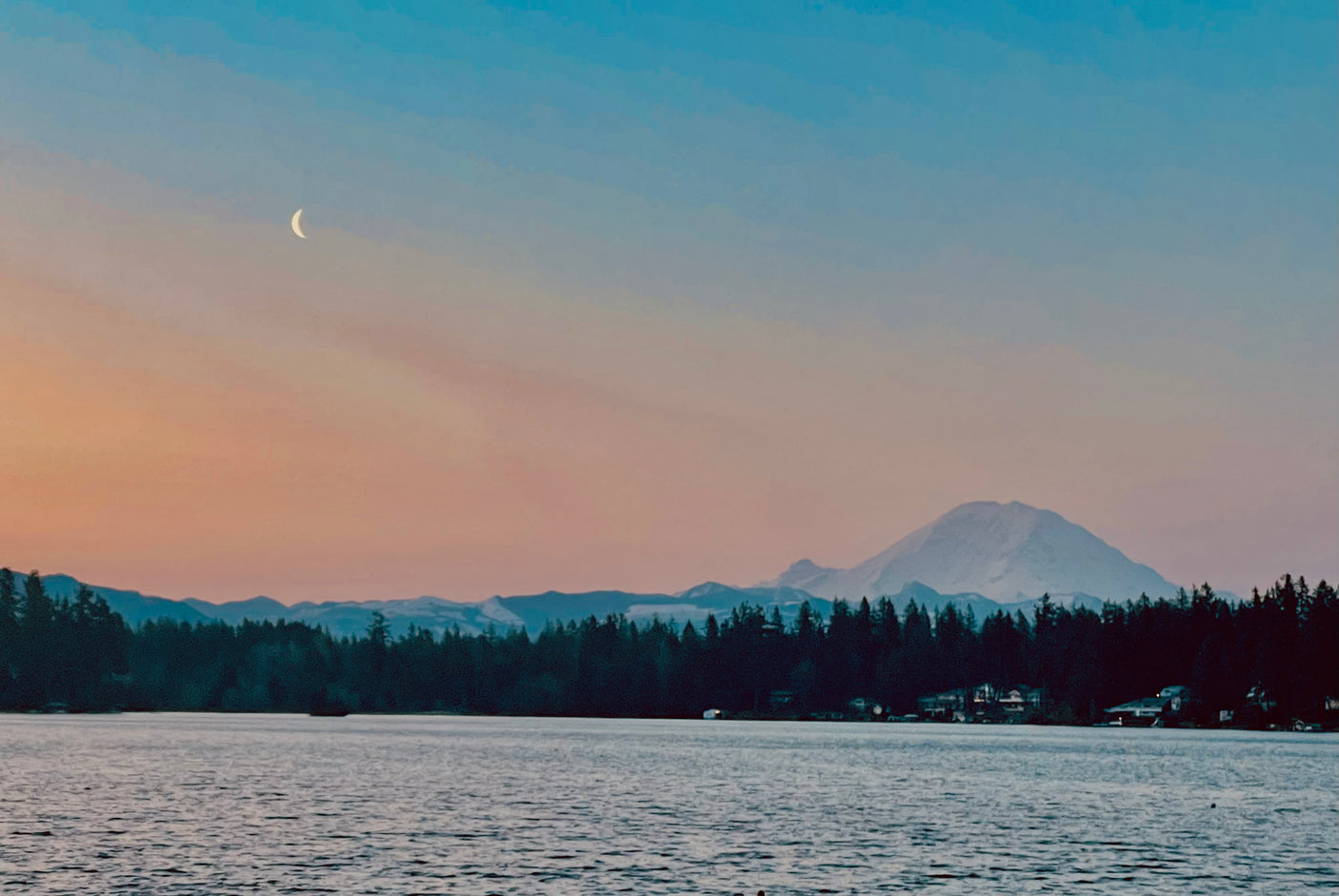 Crescent moon over a tranquil lake with Mount Rainier and forest at dusk. Plan your scenic RV rental escape.