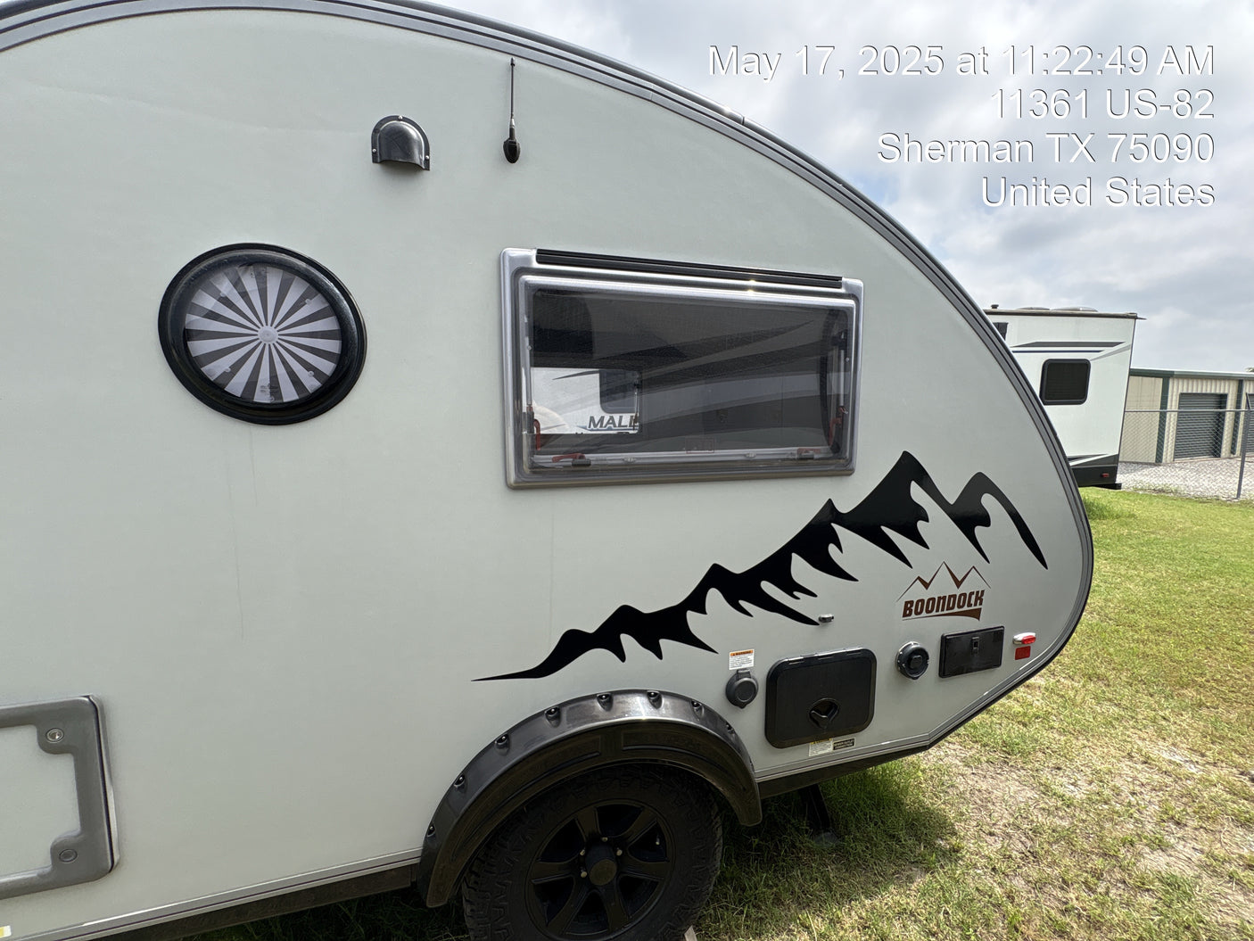 Side exterior view of a grey teardrop Boondock RV with a mountain decal. Perfect for an rv rental, parked outdoors in Sherman, TX.