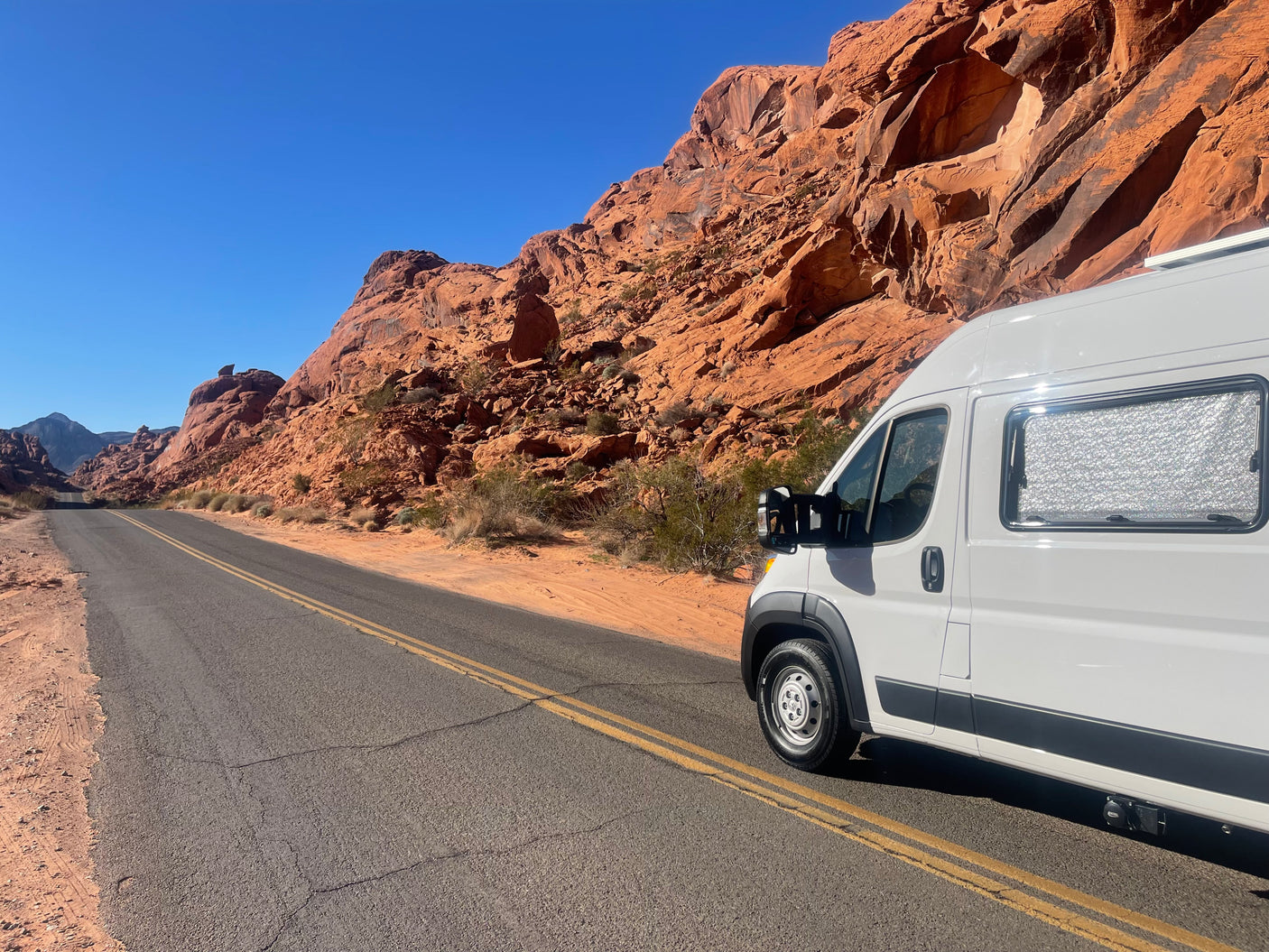 White RV rental van on a desert road alongside stunning red rock mountains, perfect for scenic travel.