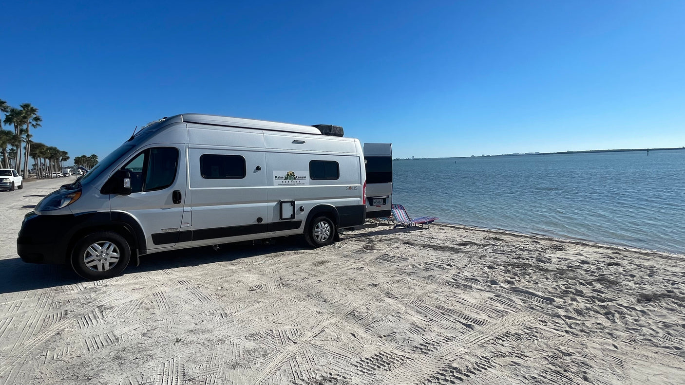 This Maine Campah rv rental van enjoys a sunny beach day by the calm blue ocean.