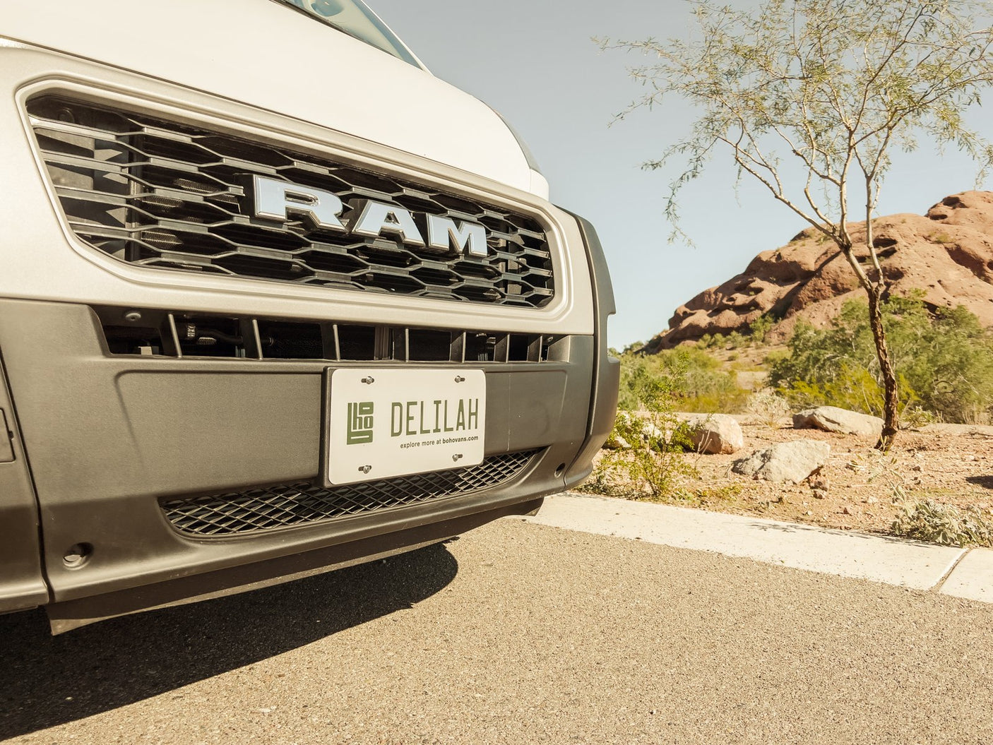 Front of a Ram ProMaster RV rental van, named "DELILAH" (Bohovans), in a sunny desert landscape.