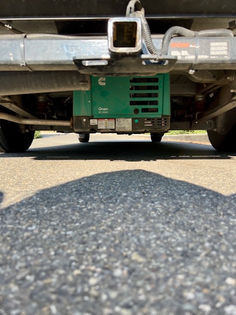 Ground-level view of a green Onan RV 2800i generator mounted under an RV rental's rear, below the tow hitch.