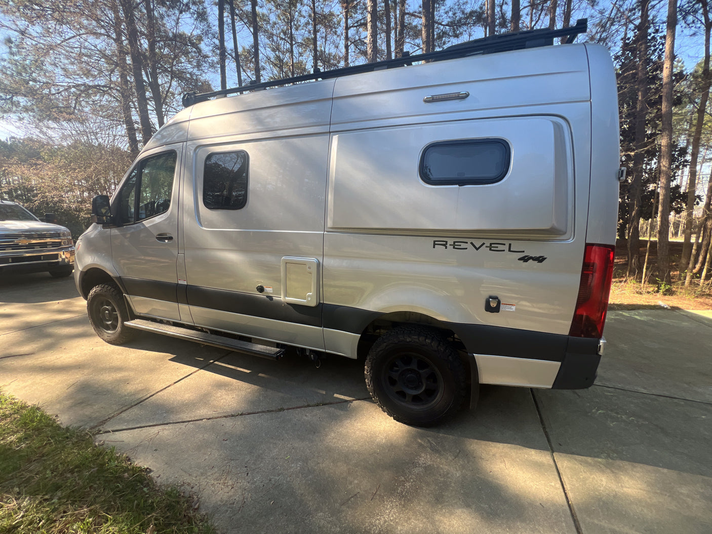 Side view of a silver Winnebago Revel 4x4 camper van on a driveway, ready for an rv rental getaway.