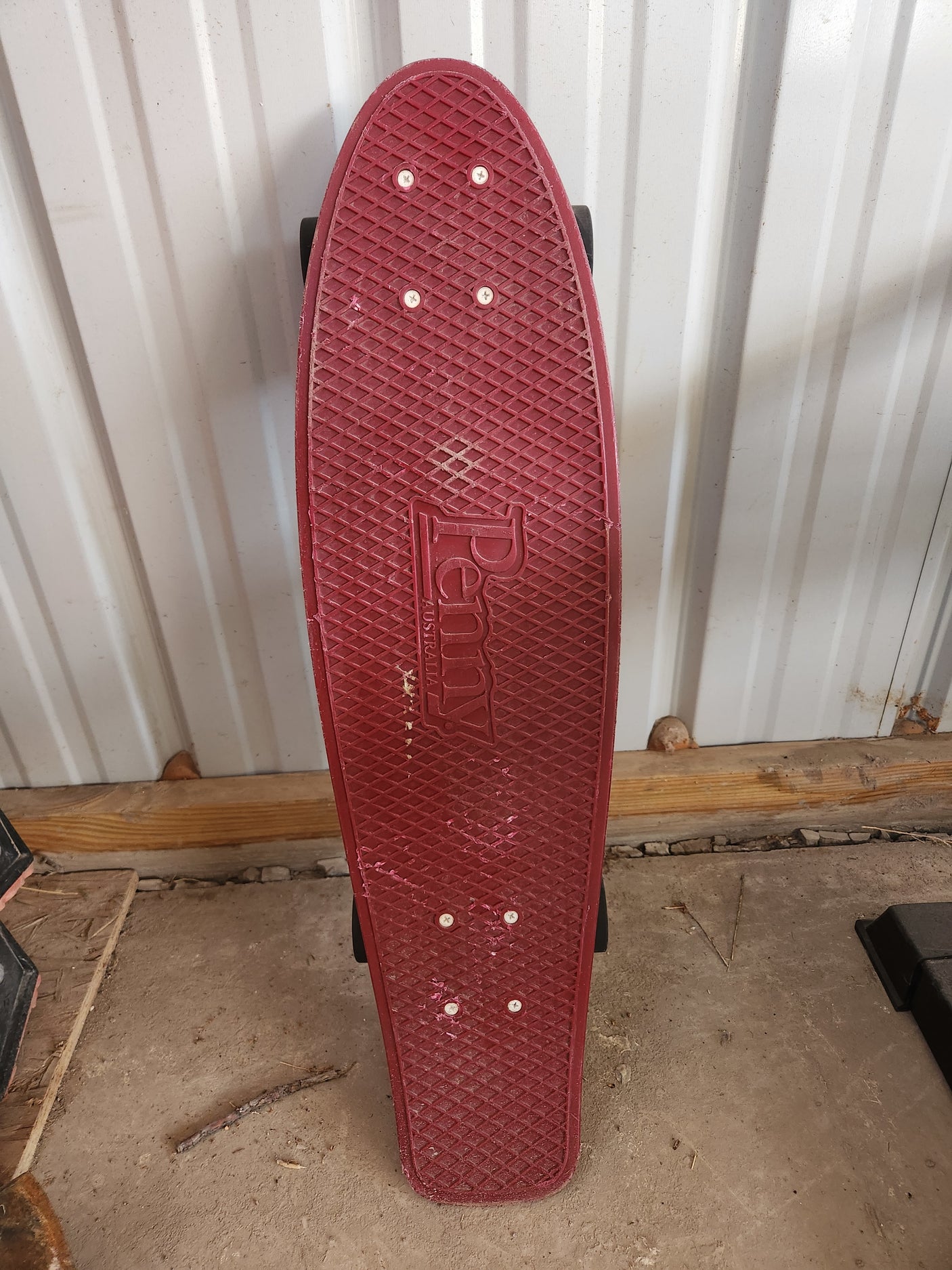 Red Penny skateboard leans by a corrugated metal shed wall, ready for an RV rental adventure or outdoor recreation.