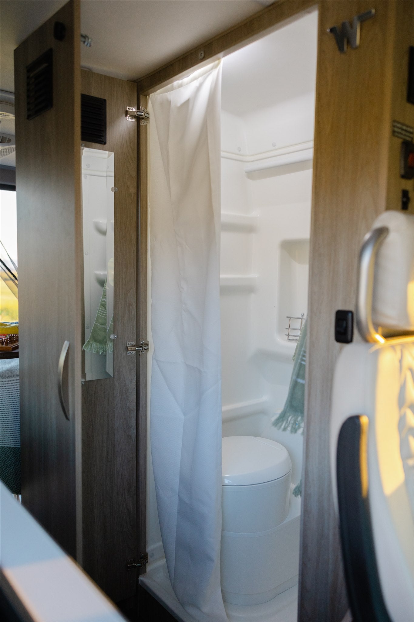 Compact RV rental bathroom with shower, toilet, and mirror, showing efficient interior design for travel.