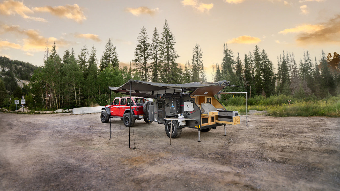 RV rental: Red Jeep with an overland camper, awning, & outdoor kitchen set up for wilderness camping in a mountain clearing.