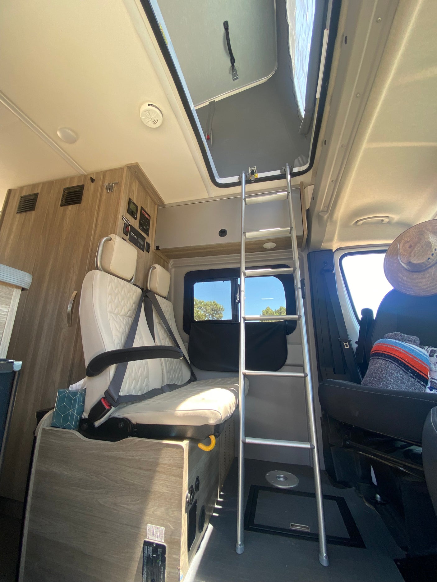Bright rv rental interior: A ladder leads to the pop-top bed, flanked by passenger seating and wood-grain cabinetry.