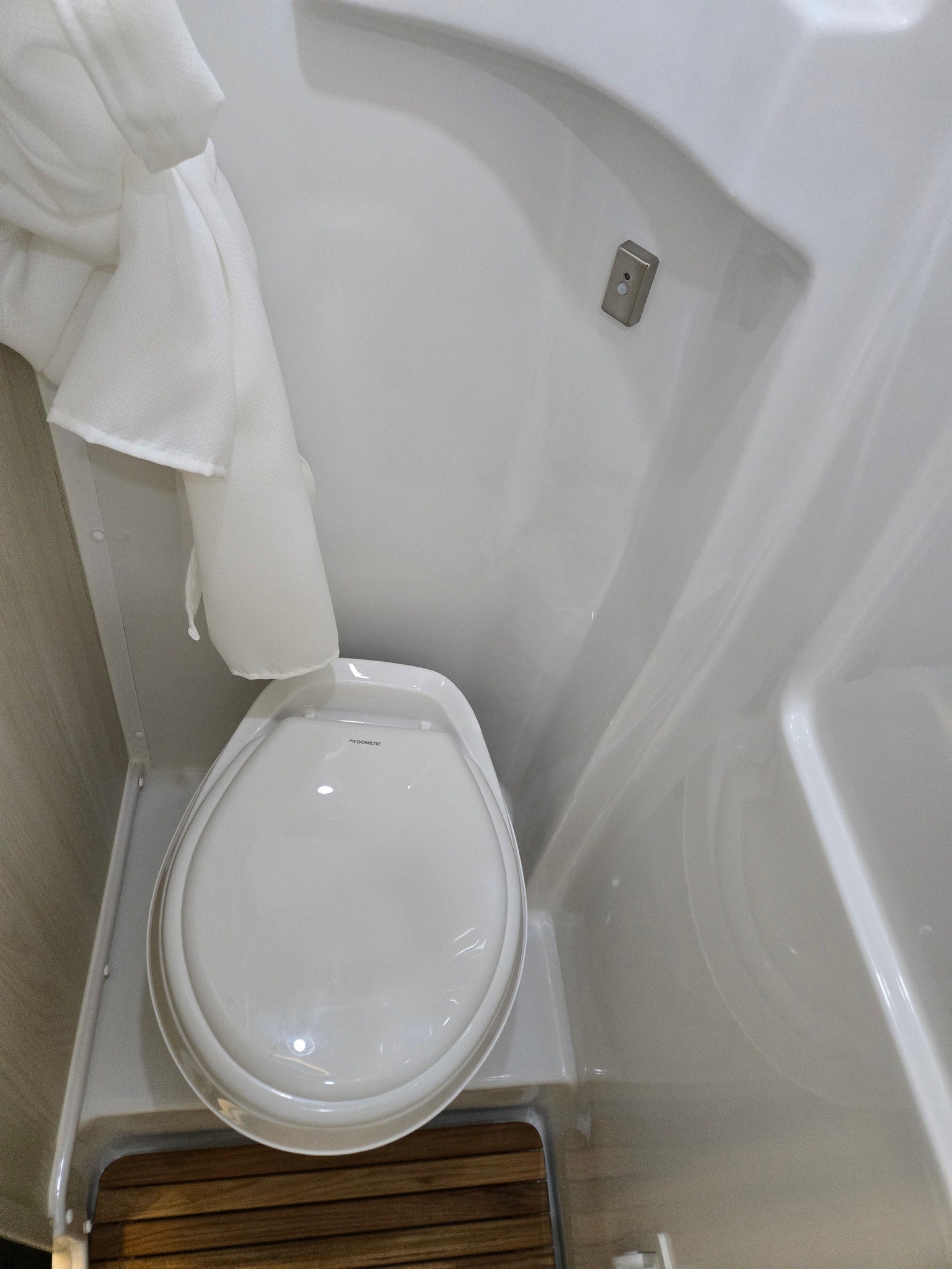 Inside an rv rental, a compact Dometic toilet is shown in a small, white wet bath with a shower curtain and slatted wood floor.