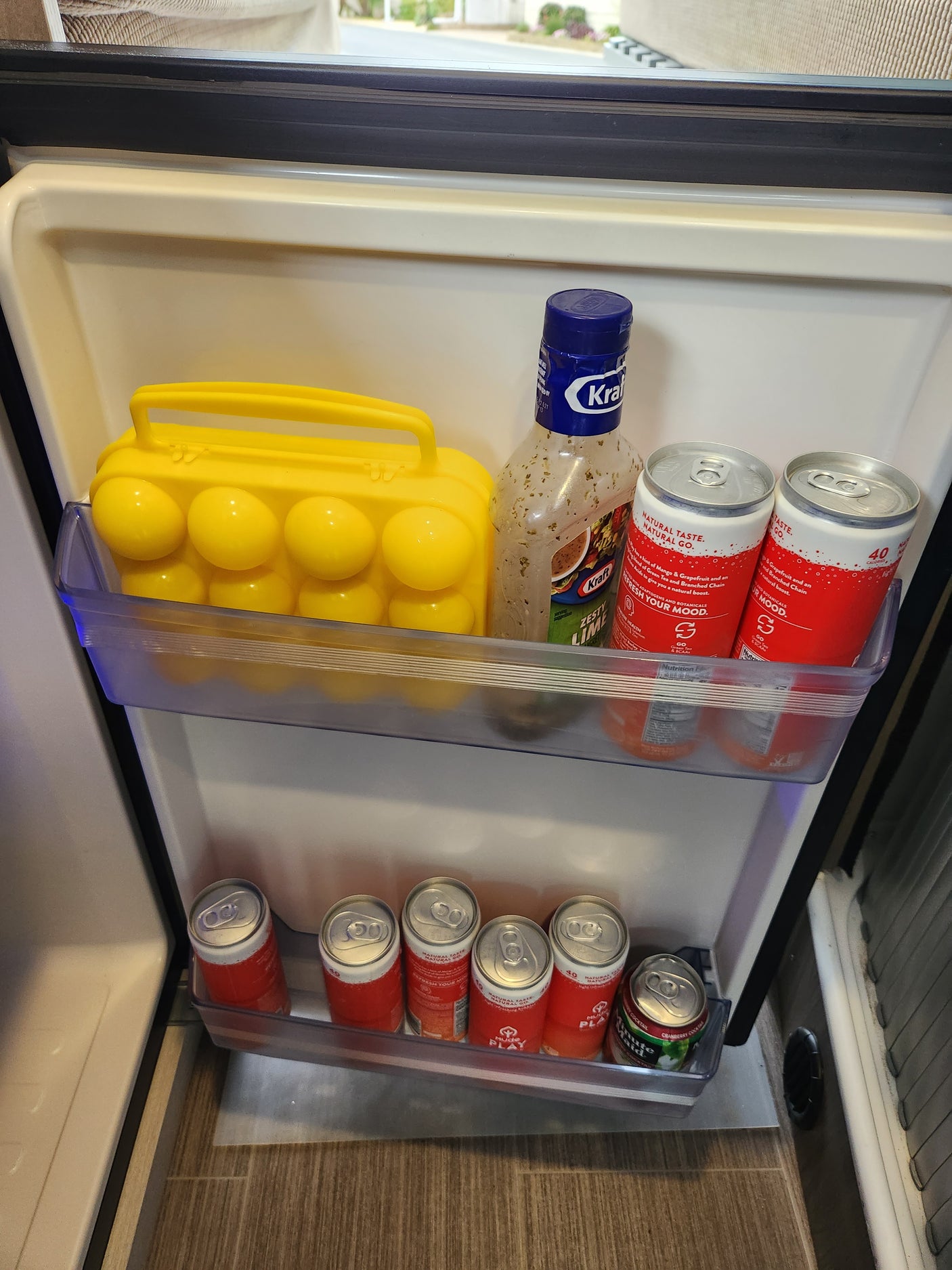 Stocked rv rental mini-fridge with Mude Play & Minute Maid drinks, Kraft dressing, and a yellow egg container.