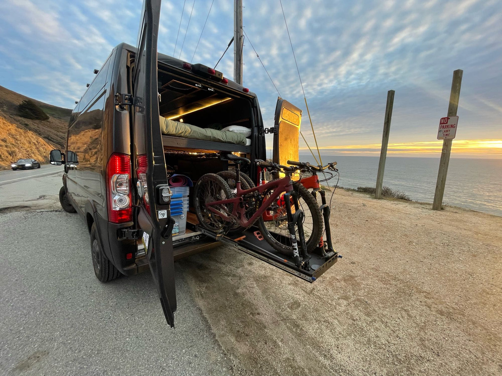 framed by spectacular red rock mountains. A digital nomad's workspace.|Workstation in a cozy RV rental: A laptop sits on a wooden desk with sleek cabinets and ambient lighting. A person is visible inside.|Dark gray Ram ProMaster van (potential RV rental) parked near striking red rock formations under a clear blue sky