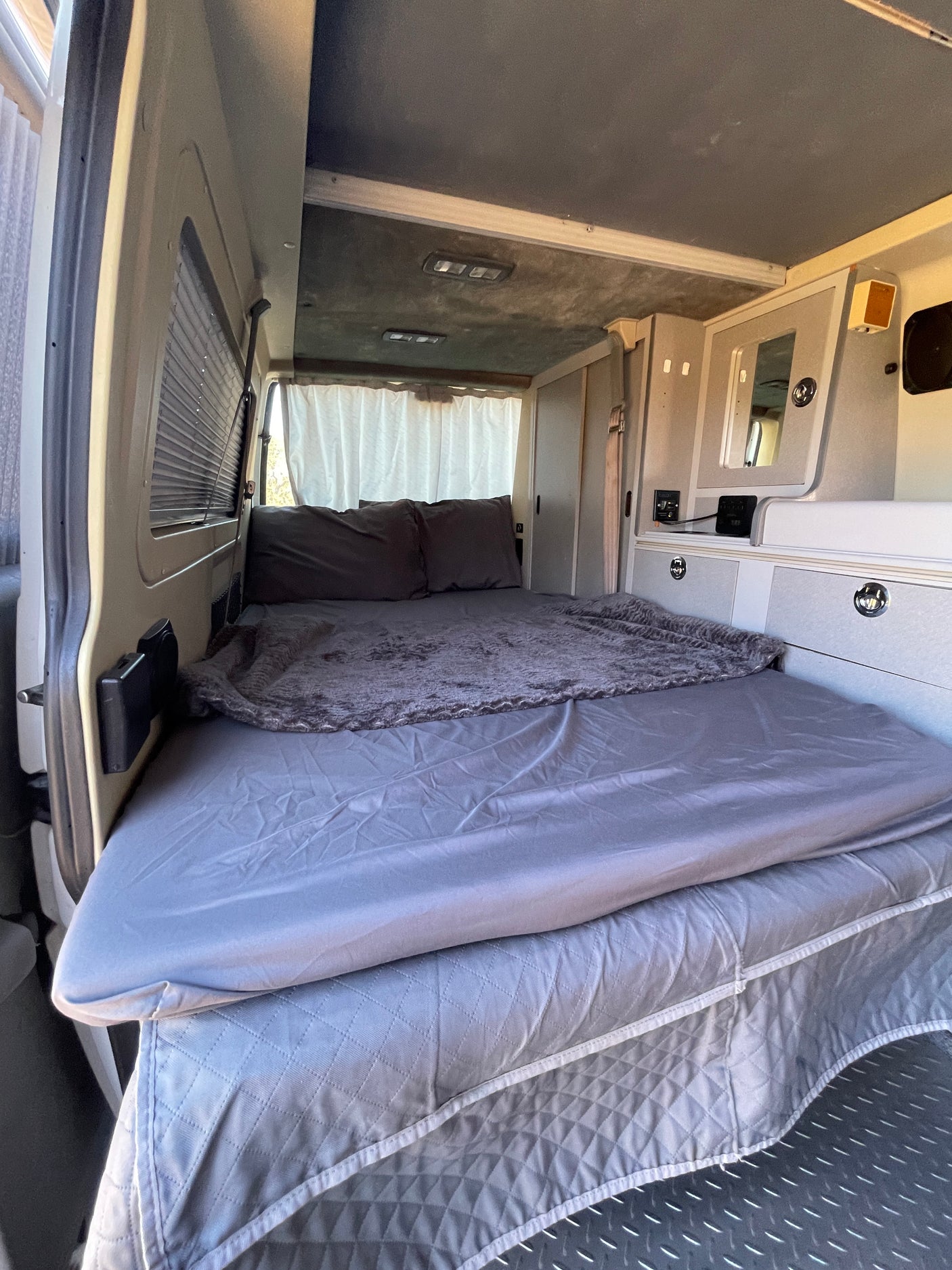 Cozy grey bed and built-in storage in this RV rental interior, with plush bedding and custom details for comfort.