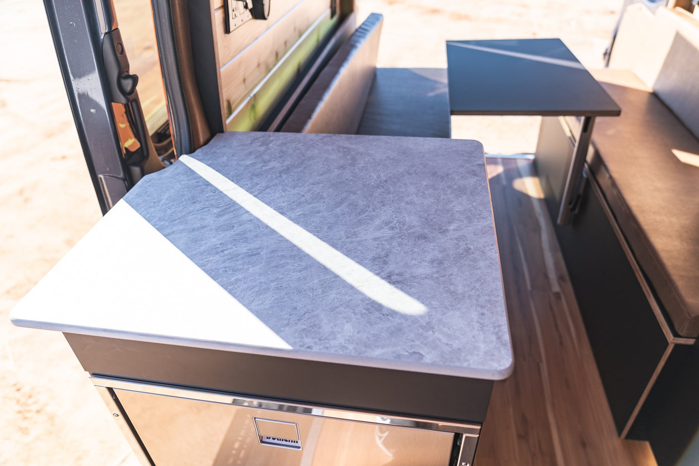 Modern RV rental interior with a compact kitchen counter, fridge, and dining area with bench seating for comfortable travel.