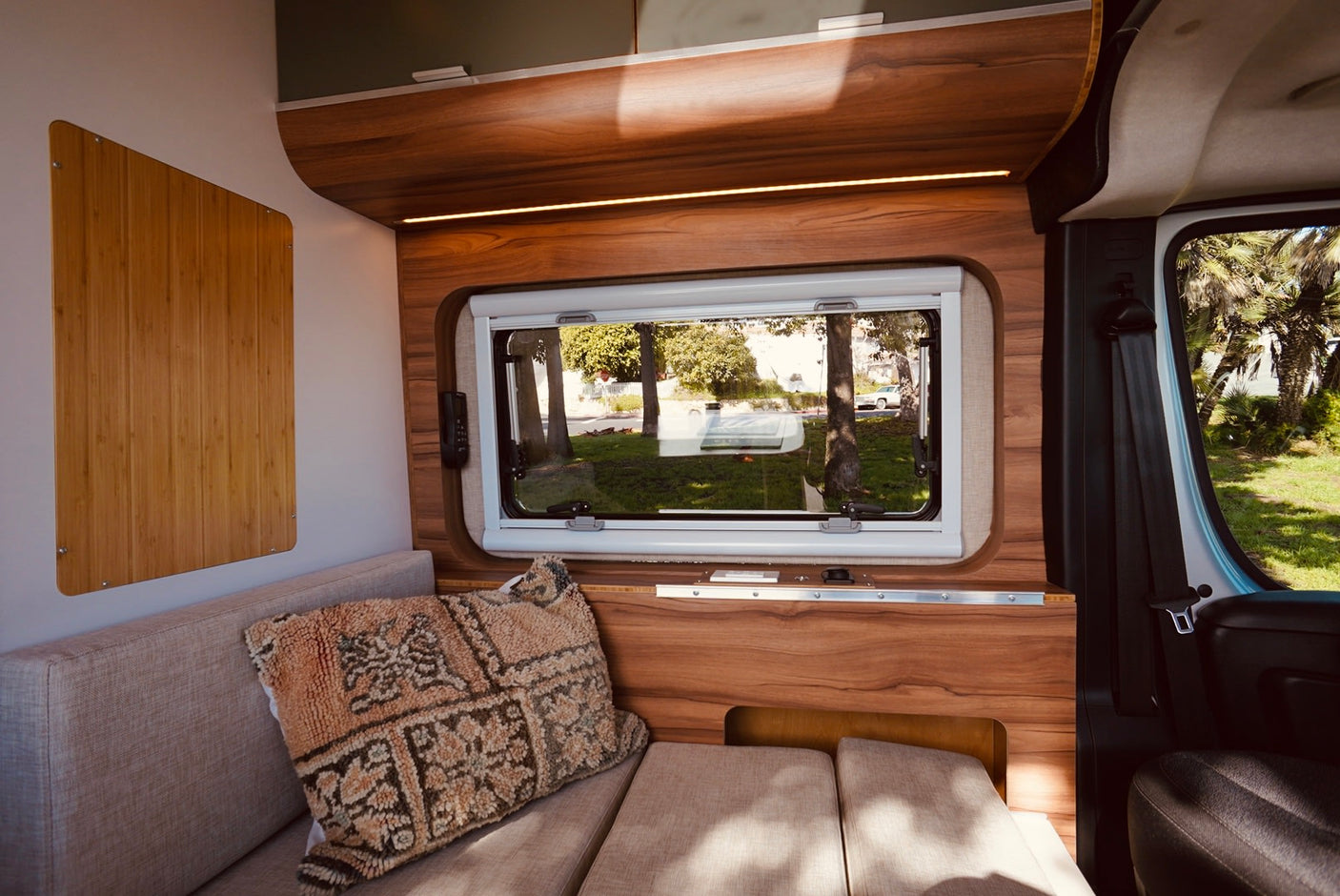 Inside a modern **rv rental**: warm wood paneling, comfy seating, and a window framing lush outdoor views.
