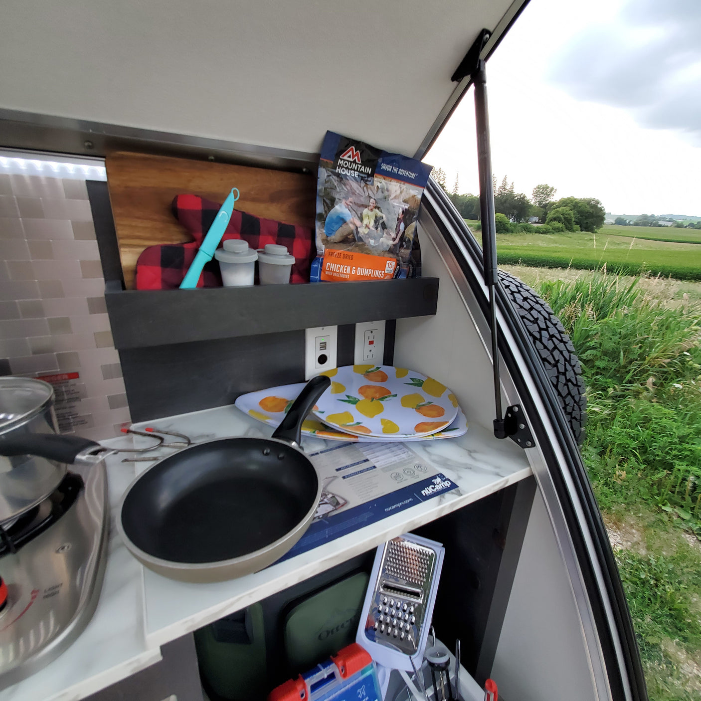 Inside an RV rental, a compact camper kitchen with a stove, cookware, and freeze-dried Chicken & Dumplings for adventure meals.