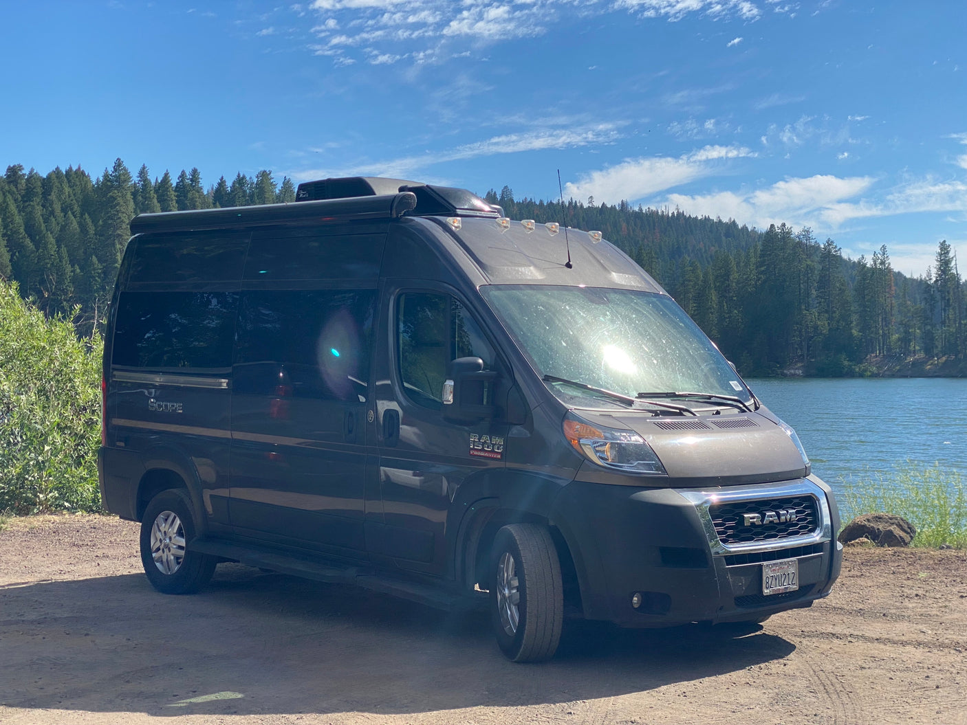 RV rental camper van parked by a serene lake with a forest background. Ready for a nature adventure.
