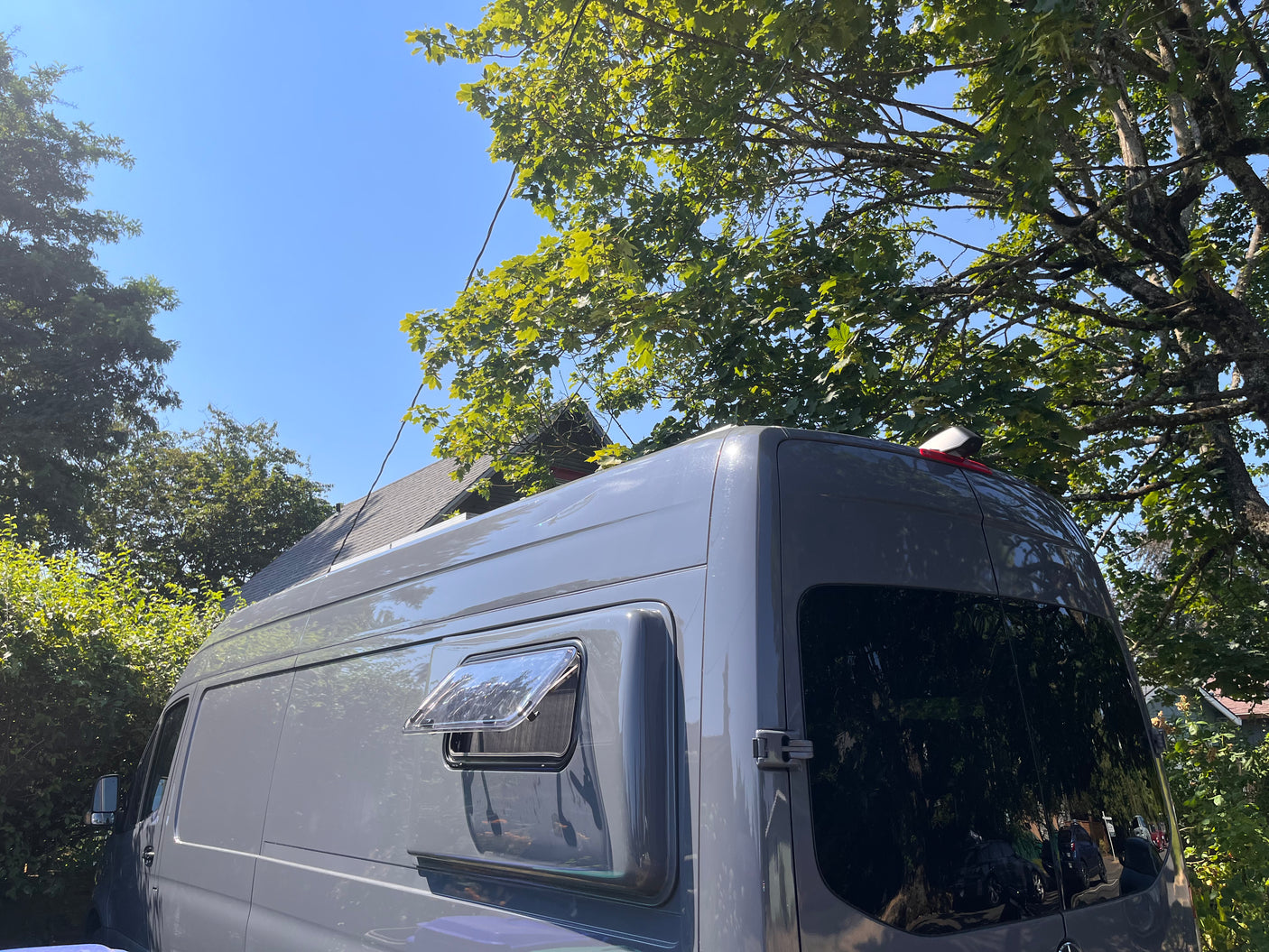 A grey camper van, an ideal rv rental, parked under trees. Its side window is open on a clear, sunny day.