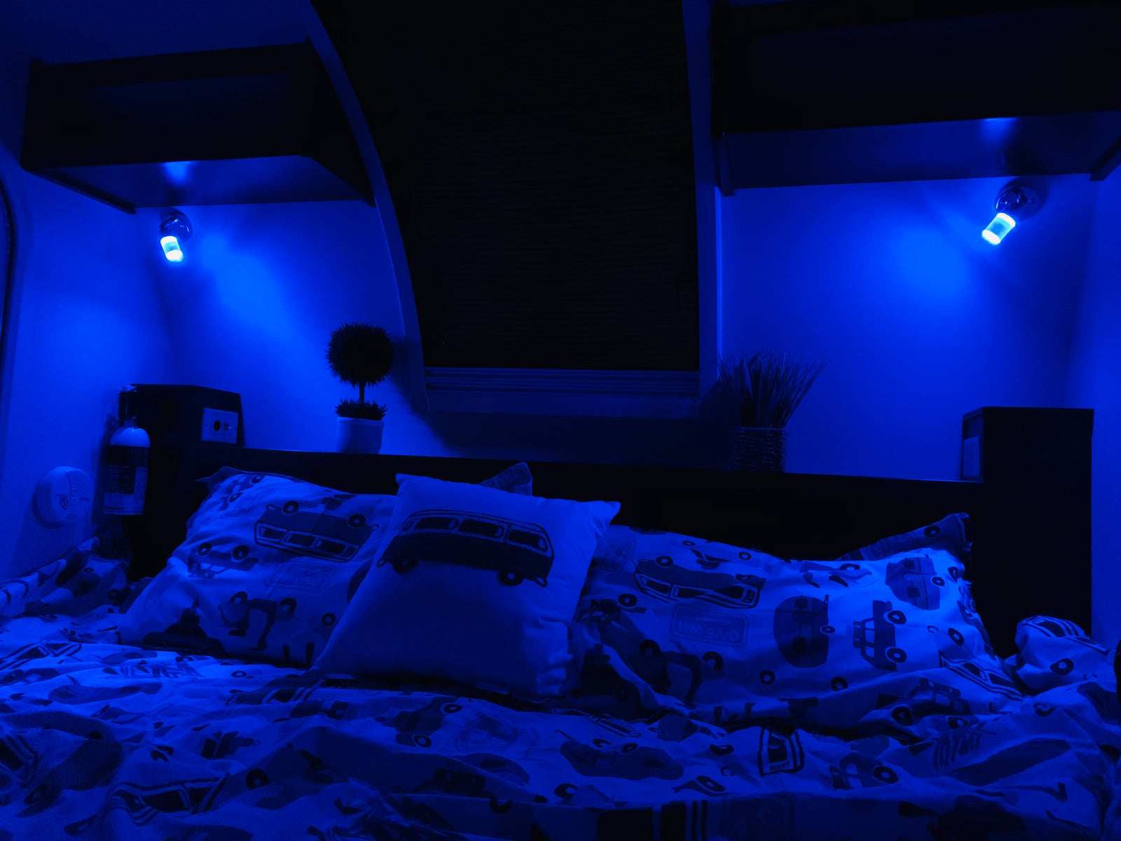 Cozy RV rental bedroom at night, featuring blue LED lighting, patterned bedding with vintage vans, and practical amenities for travel.