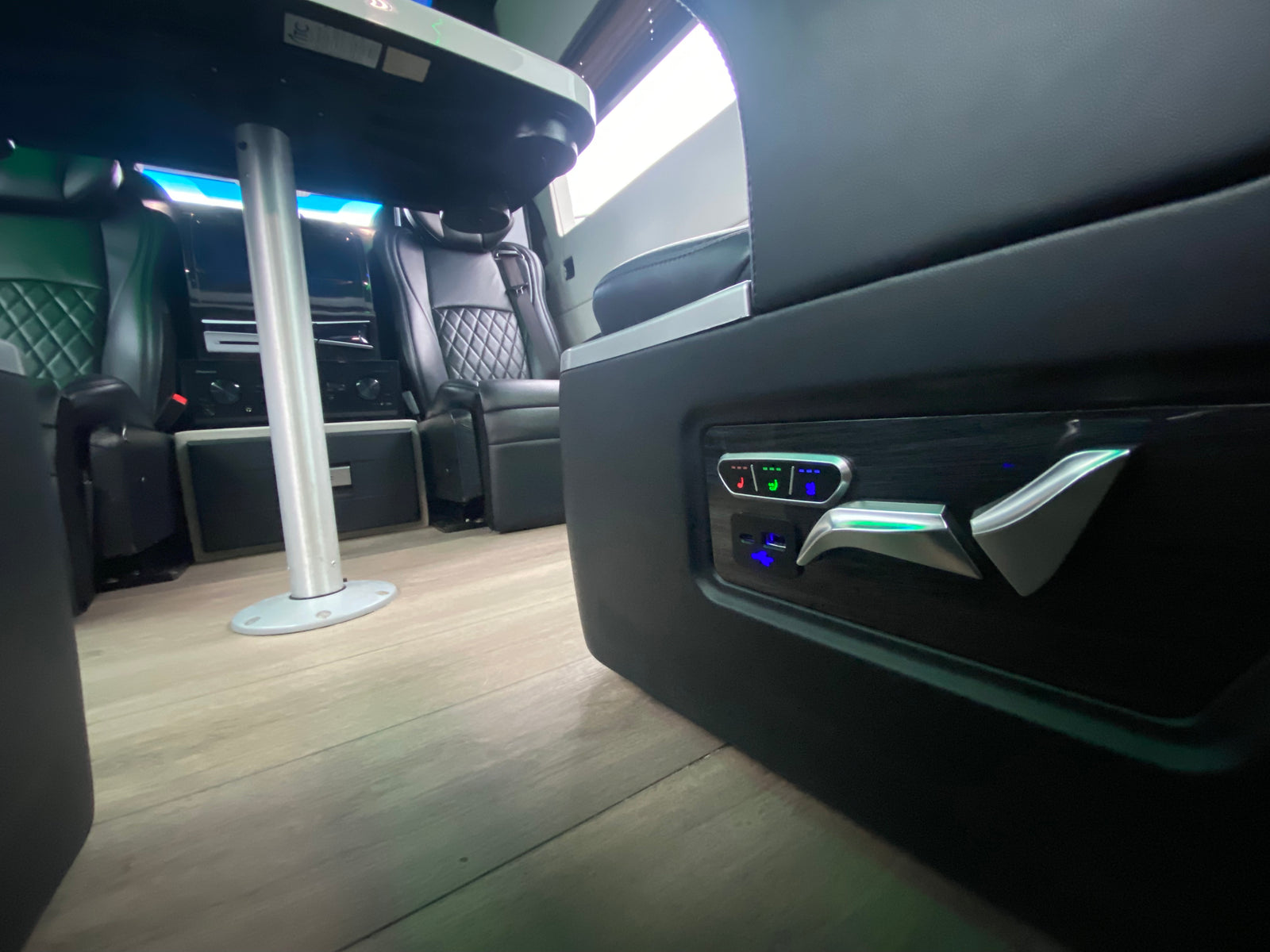 Luxury RV rental interior with illuminated seat controls, quilted seating, and a dining table.