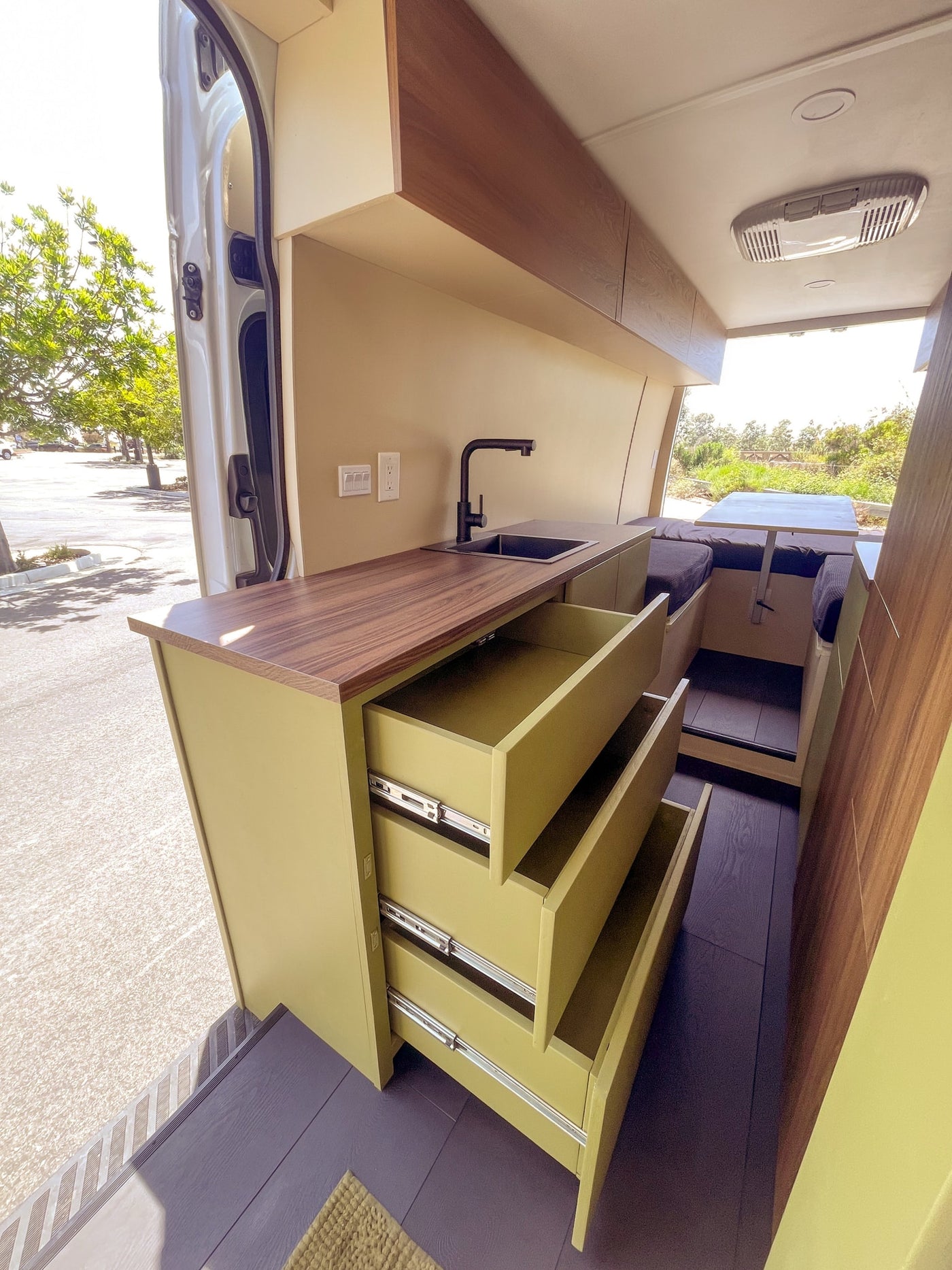 Modern RV rental interior showcases olive green drawers, wood countertop, kitchen sink, and a dinette area. — photo 7