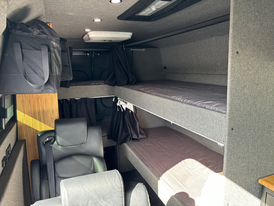 Inside this RV rental: modern camper van interior featuring bunk beds, swivel seats, overhead AC, and storage.